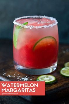 a close up of a drink in a glass on a wooden tray with limes