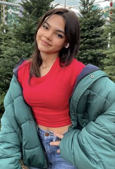 a woman in a red shirt and blue jacket standing next to trees with the words merry christmas