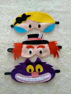 three children's masks with different faces on top of each other, one is wearing a hat and the other has an eye patch