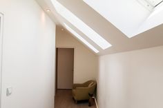 an empty room with a chair and skylight in the corner, next to a door