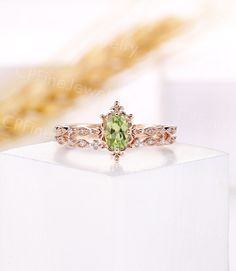 an engagement ring with a green stone surrounded by white cubicles on top of a box