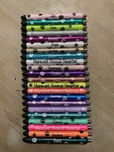 a stack of pens sitting on top of a wooden table next to a dog's paw