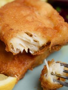 a piece of fried fish is on a plate with a fork and lemon wedges