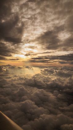 an airplane wing flying through the clouds at sunset