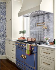 a blue stove top oven sitting inside of a kitchen next to white cabinets and drawers