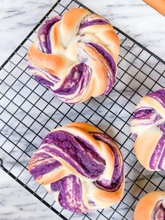 four purple swirled doughnuts on a cooling rack next to an orange and white towel