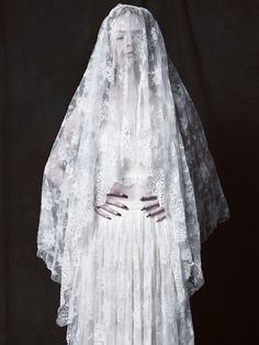 a woman wearing a white wedding dress and veil with her hands on her hips, standing in front of a black background