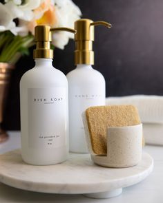 two soap dispensers sitting on top of a white marble plate next to a gold faucet