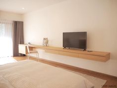 a flat screen tv sitting on top of a wooden shelf next to a white bed