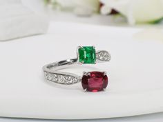 an emerald and ruby ring with diamond accents on a white plate next to a flower