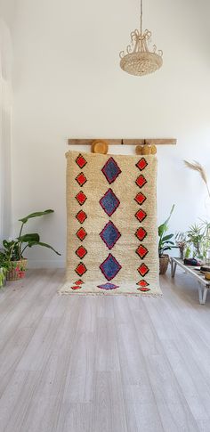 a rug hanging on a wall in a room with wooden floors and plants around it