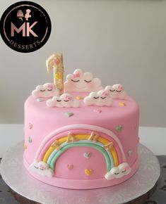 a pink cake decorated with clouds, rainbows and a number one on the top