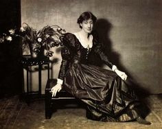 an old black and white photo of a woman in a dress sitting on a chair