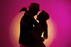 a man and woman dance in front of a pink background with the sun behind them