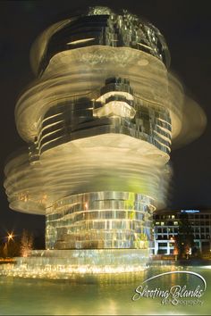 a very tall building with lots of lights on it's sides and water in the foreground