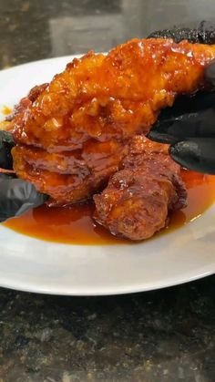 a white plate topped with meat covered in sauce on top of a counter next to black gloves