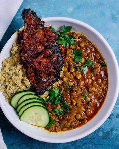 a white plate topped with meat and beans next to cucumber on top of rice