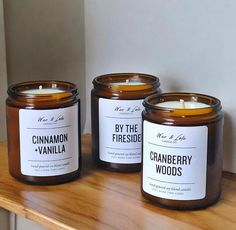 three candles sitting on top of a wooden table next to each other with labels reading by the fireside and cranberry woods