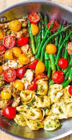 a pan filled with pasta, asparagus and tomatoes