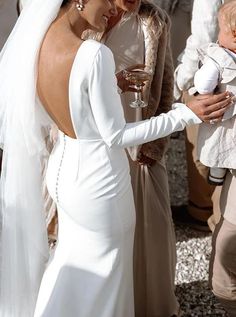 a woman in a white dress holding a baby next to other people and wine glasses