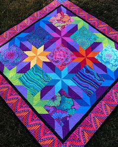 a multicolored quilt on the ground with grass in the backgroung