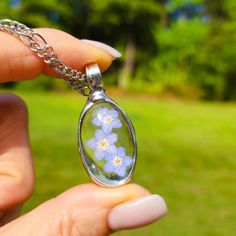 If you're looking for a thoughtful jewelry gift for mom, this real pressed flower necklace is a perfect choice. It features an authentic forget me not pendant set in stained glass terrarium jewelry that's both beautiful and meaningful. It's a lovely mother's day keepsake that she'll treasure for years to come. I have made glass pendants with forget me nots for years but never have I placed blooms in an oval shape. Oversight I guess as I think the cascade of blooms is both feminine and makes for Silver Jewelry With Pressed Flowers For Mother's Day, Memorial Birth Flower Jewelry, Pressed Flowers Flower Pendant Jewelry For Mother's Day, Silver Pressed Flowers Memorial Jewelry, Pressed Flower Pendant Jewelry For Mother's Day, Silver Pressed Flowers Jewelry For Memorial, Pressed Flowers Jewelry For Mother's Day Gift, Mother's Day Pressed Flower Pendant Necklace, Silver Memorial Jewelry With Pressed Flowers