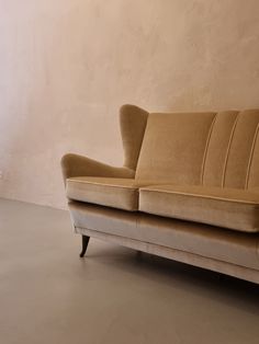 a tan couch sitting on top of a hard wood floor next to a white wall