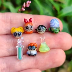 a hand holding five little toy figurines in it's palm, with plants behind them