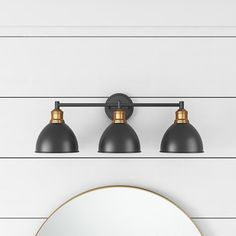 three light bathroom fixture with black shade shades on the wall and round mirror above it