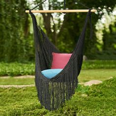 a black hammock hanging from a wooden pole with two pillows on it in the grass