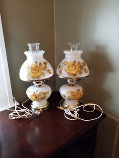 two white vases sitting on top of a wooden table next to each other with yellow flowers painted on them