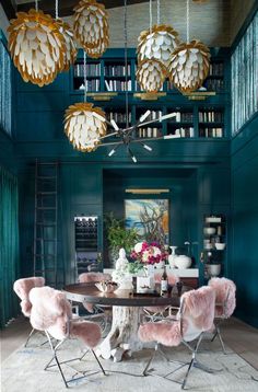 a dining room with blue walls and chandeliers hanging from the ceiling, along with pink chairs