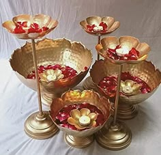 four gold bowls with flowers in them on a white background, one is filled with water and the other has candles