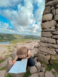 a woman sitting on top of a rocky hill writing