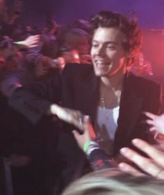 a man in a black suit and white shirt at a concert with his hands out