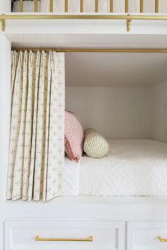 a white bed sitting under a window next to a curtain and pillow on top of it