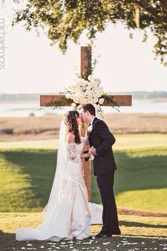 a bride and groom kissing in front of a cross