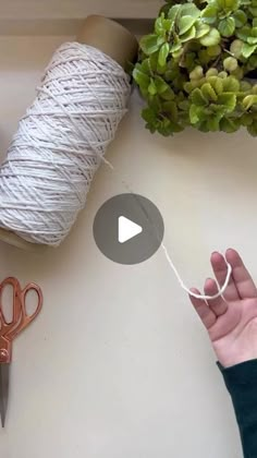 someone is stringing up some yarn on a table with scissors and a potted plant in the background