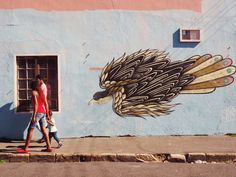 a woman and child walking past a painted eagle on the side of a blue building