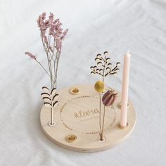 two candles and some flowers are on a table with a name plate in the middle