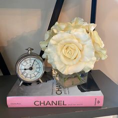 a white rose sitting on top of a book next to an alarm clock and a pink book