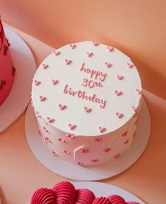 a birthday cake with pink frosting and hearts on the top is sitting next to two other cakes