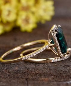 two gold rings with an emerald and diamond set on top of each other next to yellow flowers