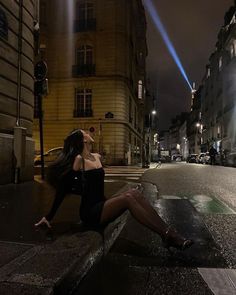 a woman sitting on the side of a road next to a traffic light at night