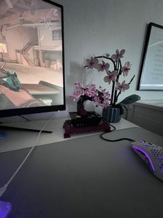 a desk with a computer monitor, keyboard and mouse on top of it next to a vase with flowers