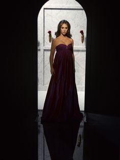 a woman in a long dress standing next to a wall