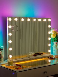 an illuminated vanity mirror sitting on top of a table next to a vase with flowers