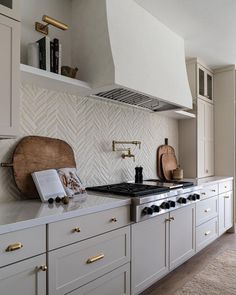 a kitchen with white cabinets and gold handles on the stove top, along with a wooden cutting board