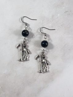 These Thanatos themed earrings are the perfect accessory to show your love for the Greek gods in a subtle way! Made with obsidian gemstone and a grim reaper charm. Made with hypoallergenic fishhook style earrings. Two options are available: Stainless Steel Silver Plated Brass Ships in a jewelry box so it's ready to be give as a gift. All materials are lead and nickel free. Charm is made with zinc alloy. Earrings will be disinfected before shipment but should also be cleaned every time before wea Handmade Symbolic Black Earrings, Witchy Pierced Earrings As Gift, Pierced Witchy Earrings For Gift, Witchy Style Pierced Earrings As Gift, Witchy Style Pierced Earrings For Gift, Symbolic Black Earrings For Gift, Mystical Black Metal Earrings, Nickel Free Sterling Silver Witchy Earrings, Nickel-free Sterling Silver Witchy Earrings