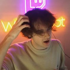 a young man is brushing his hair in front of a neon sign